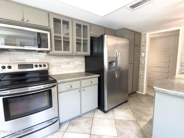 7770 E Camelback Rd Unit 23, Scottsdale, AZ 85251 - kitchen with appliances with stainless steel finishes, gray cabinetry, light tile patterned floors, glass insert cabinets, and decorative backsplash