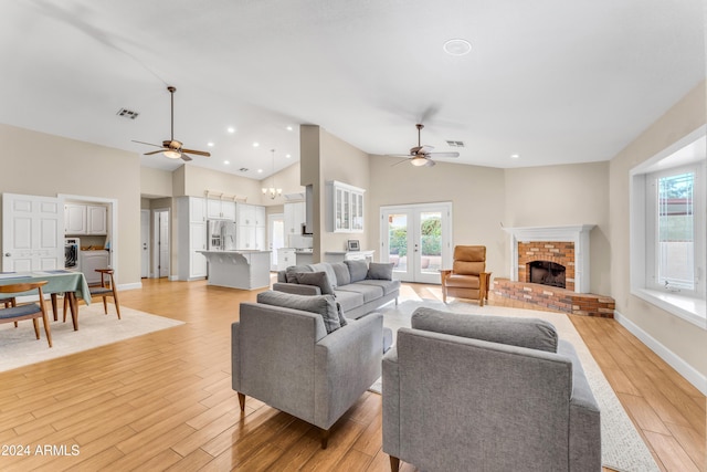 living room with ceiling fan, french doors, a brick fireplace, high vaulted ceiling, and light wood-type flooring