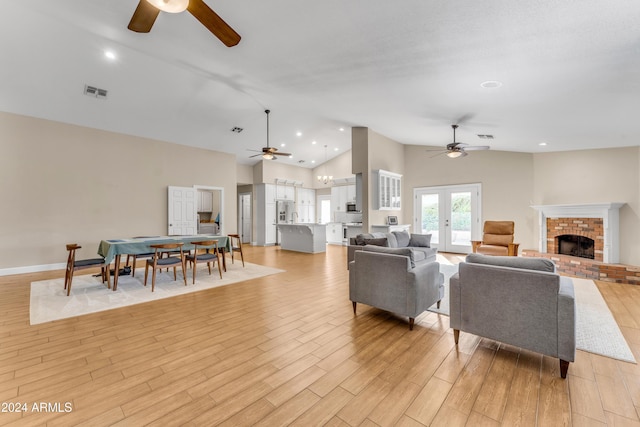 living room featuring high vaulted ceiling, french doors, a brick fireplace, ceiling fan, and light hardwood / wood-style floors