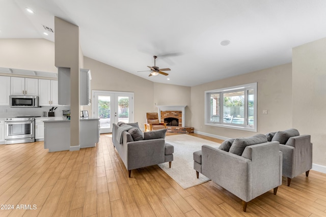 living room featuring ceiling fan, french doors, a brick fireplace, light hardwood / wood-style flooring, and lofted ceiling