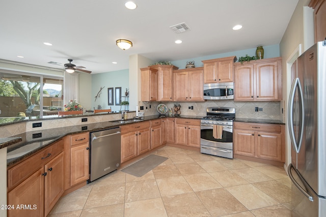 kitchen featuring ceiling fan, dark stone counters, decorative backsplash, light tile patterned floors, and appliances with stainless steel finishes