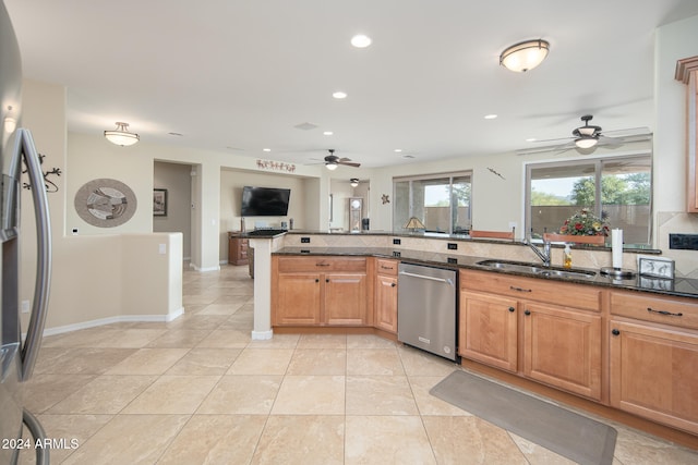 kitchen with sink, ceiling fan, dark stone countertops, appliances with stainless steel finishes, and kitchen peninsula