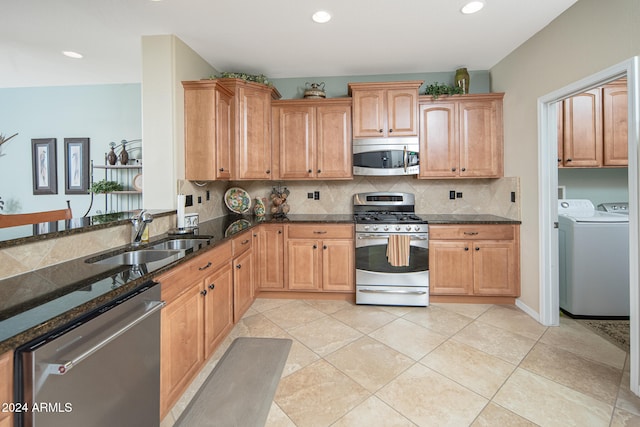 kitchen featuring dark stone counters, sink, washing machine and dryer, appliances with stainless steel finishes, and tasteful backsplash