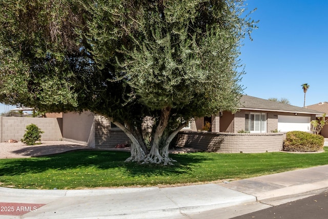 view of property hidden behind natural elements featuring a front yard, brick siding, and fence