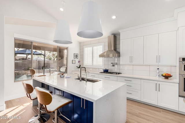 kitchen featuring a sink, tasteful backsplash, appliances with stainless steel finishes, wall chimney range hood, and vaulted ceiling