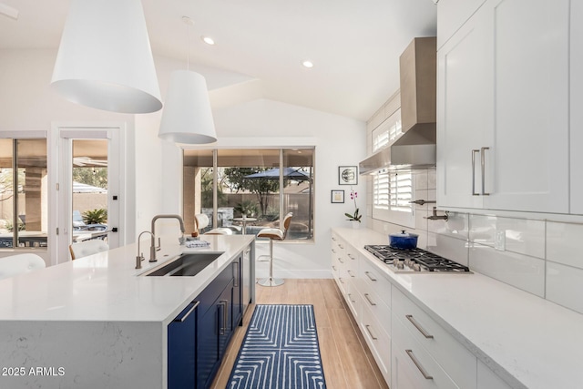 kitchen featuring wall chimney range hood, light countertops, vaulted ceiling, stainless steel gas stovetop, and a sink