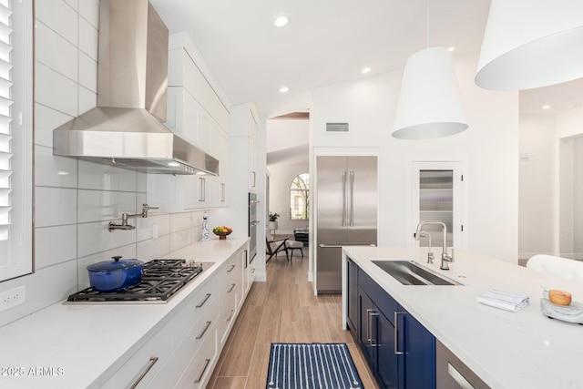 kitchen featuring a sink, wall chimney range hood, white cabinetry, stainless steel appliances, and light countertops