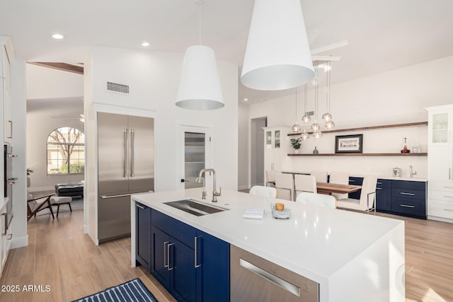 kitchen featuring blue cabinets, light wood-style flooring, a sink, open shelves, and built in fridge