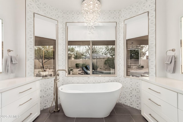 bathroom featuring vanity, wallpapered walls, an inviting chandelier, a freestanding tub, and tile patterned floors