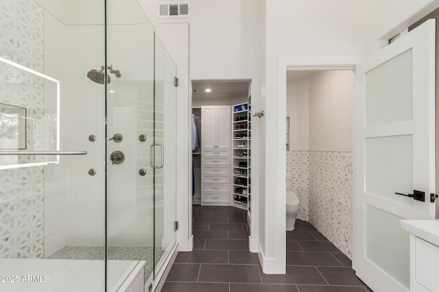 full bath featuring visible vents, a walk in closet, toilet, a shower stall, and tile patterned flooring