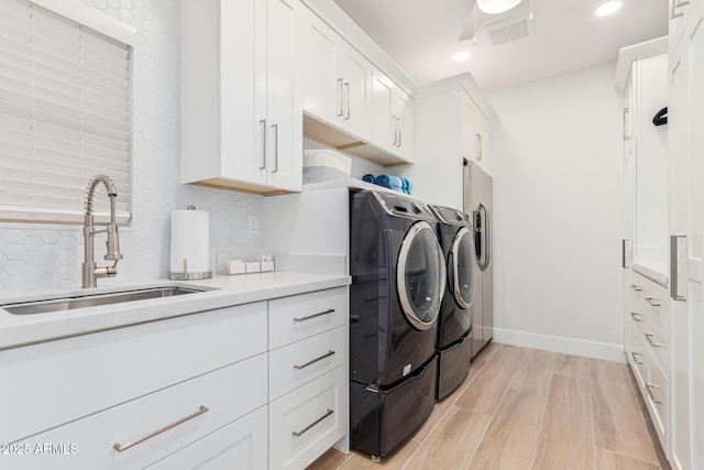 laundry area with visible vents, light wood-style flooring, cabinet space, a sink, and washer and dryer