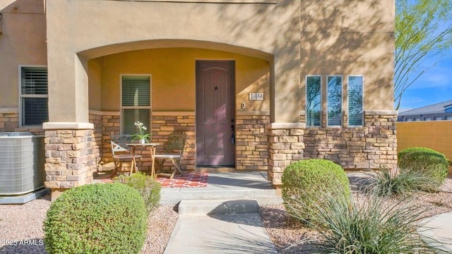 entrance to property featuring stone siding, cooling unit, and stucco siding