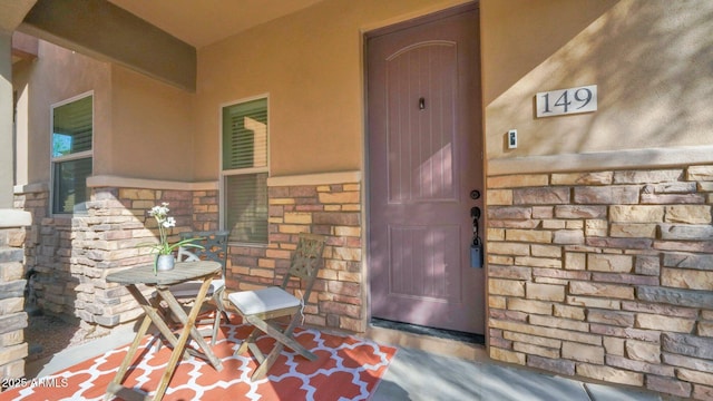 doorway to property with a porch, stone siding, and stucco siding