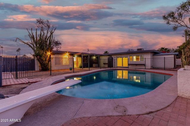 pool at dusk with a patio area and a diving board