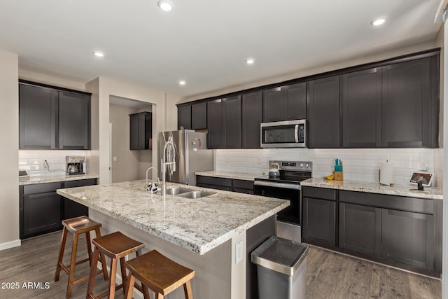 kitchen featuring appliances with stainless steel finishes, a kitchen breakfast bar, light stone counters, a center island with sink, and dark hardwood / wood-style flooring