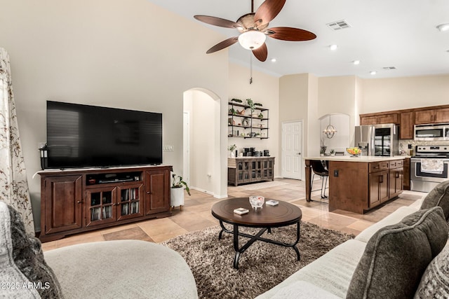 living area with arched walkways, high vaulted ceiling, ceiling fan, baseboards, and light tile patterned floors
