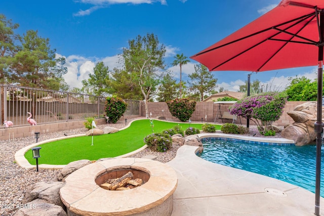 view of pool with an area to practice putting, a fenced backyard, an outdoor fire pit, and a patio