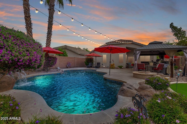 pool at dusk featuring a patio area, a gazebo, and a fenced backyard