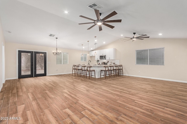 unfurnished living room featuring visible vents, vaulted ceiling, light wood finished floors, and ceiling fan with notable chandelier