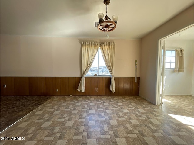 empty room with an inviting chandelier and wood walls