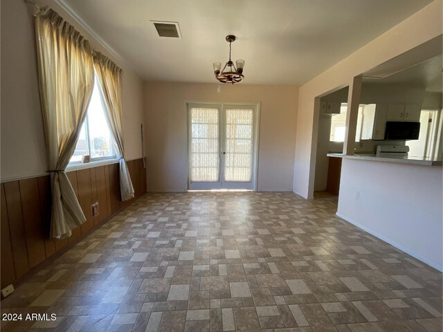 interior space with french doors, wooden walls, and a notable chandelier