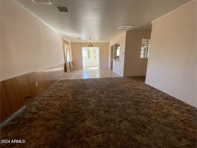 empty room with carpet flooring, wooden walls, and a notable chandelier