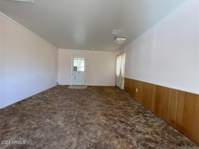 carpeted empty room featuring ornamental molding and wood walls