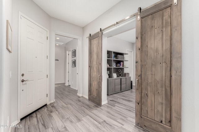 hallway featuring a barn door, light wood-style flooring, and baseboards