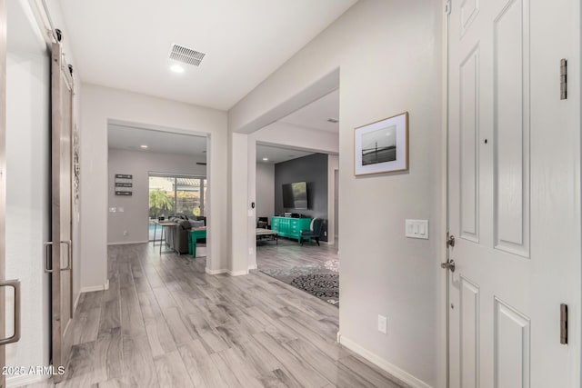 entryway with baseboards, visible vents, light wood finished floors, and a barn door