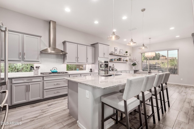 kitchen featuring gray cabinets, backsplash, appliances with stainless steel finishes, a sink, and wall chimney exhaust hood