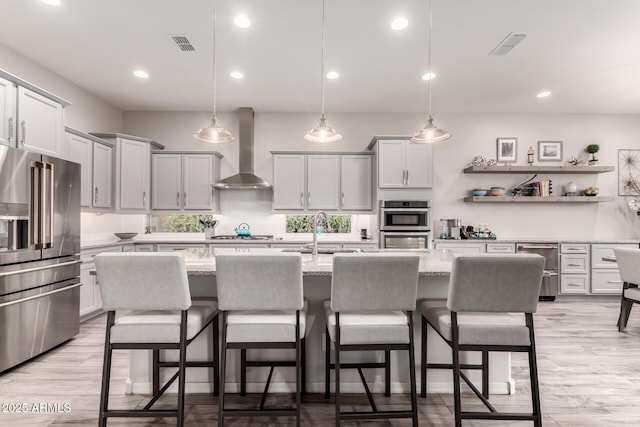 kitchen with a breakfast bar area, a sink, visible vents, appliances with stainless steel finishes, and wall chimney range hood