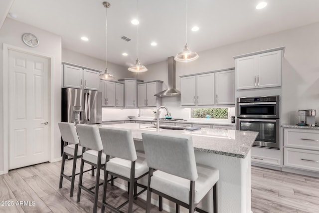 kitchen featuring appliances with stainless steel finishes, pendant lighting, wall chimney range hood, and a kitchen breakfast bar