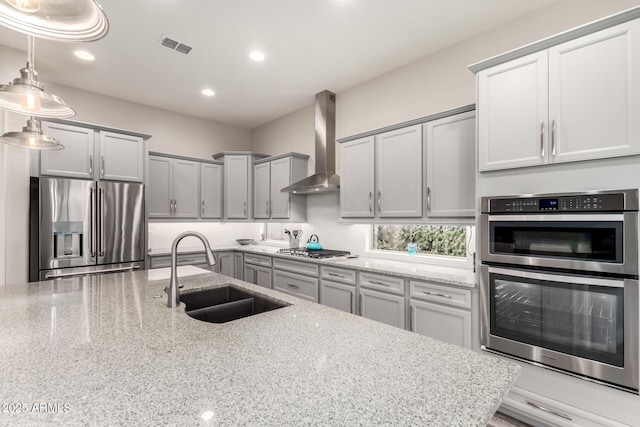 kitchen featuring wall chimney exhaust hood, appliances with stainless steel finishes, gray cabinets, and a sink