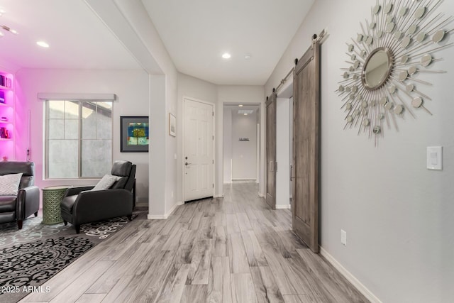 hall with light wood-style floors, a barn door, baseboards, and recessed lighting