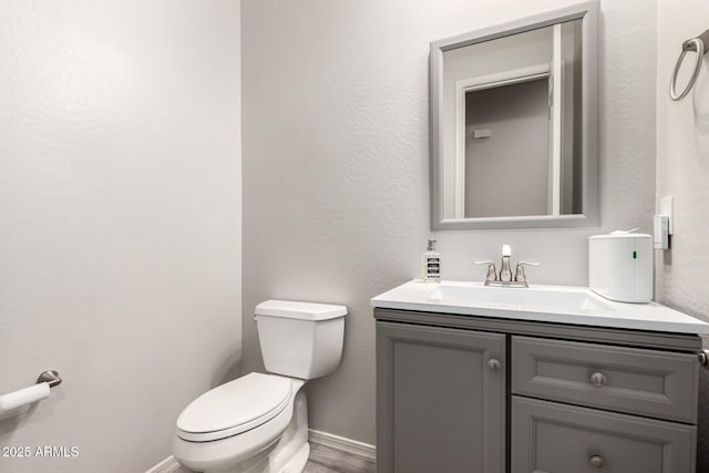 half bath with baseboards, a textured wall, toilet, wood finished floors, and vanity