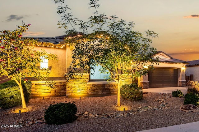 view of front facade featuring stone siding, concrete driveway, an attached garage, and stucco siding