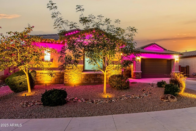 view of front facade featuring driveway, stone siding, a garage, and stucco siding