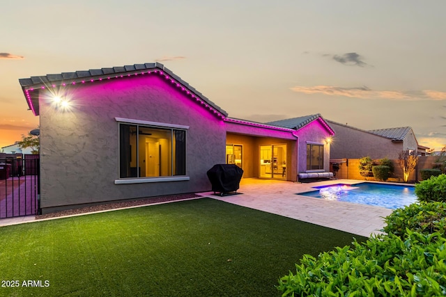 back of house at dusk with a fenced in pool, a patio, stucco siding, a lawn, and fence