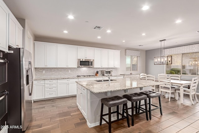 kitchen with white cabinets, appliances with stainless steel finishes, sink, hanging light fixtures, and a kitchen island with sink