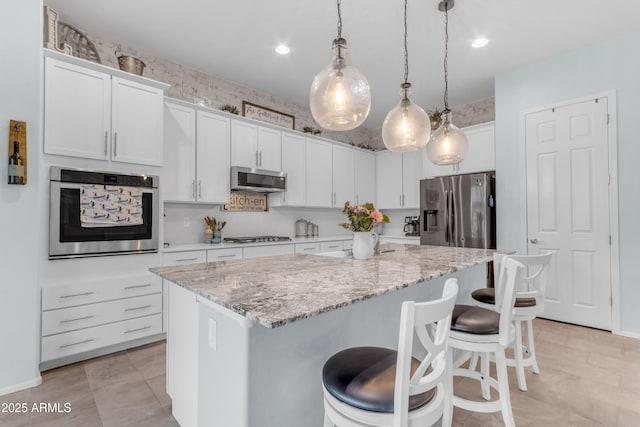 kitchen with appliances with stainless steel finishes, a center island, a kitchen breakfast bar, white cabinetry, and pendant lighting