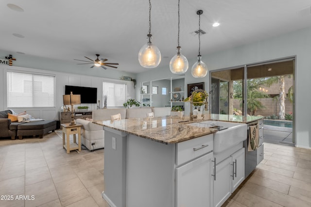 kitchen featuring open floor plan, a center island with sink, light stone countertops, hanging light fixtures, and healthy amount of natural light
