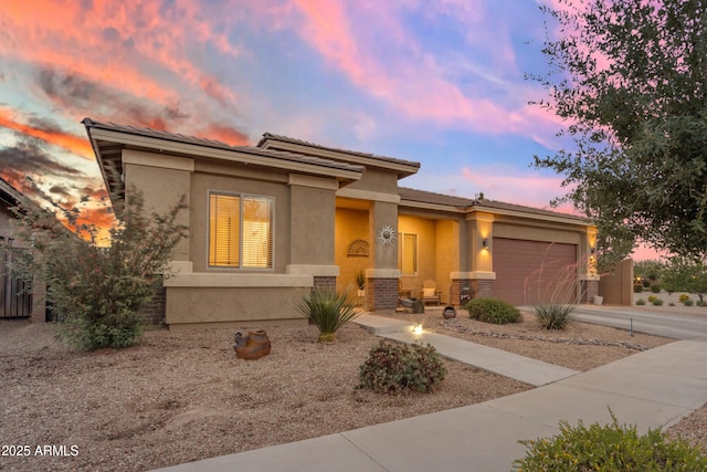 prairie-style house featuring an attached garage, stucco siding, driveway, and brick siding