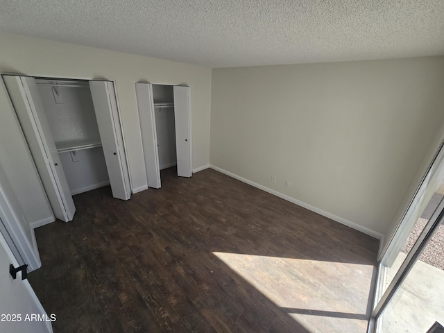 unfurnished bedroom featuring two closets, dark wood-type flooring, and a textured ceiling