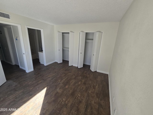 unfurnished bedroom featuring dark hardwood / wood-style flooring, two closets, and a textured ceiling