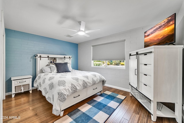 bedroom featuring ceiling fan, a barn door, brick wall, and dark hardwood / wood-style flooring