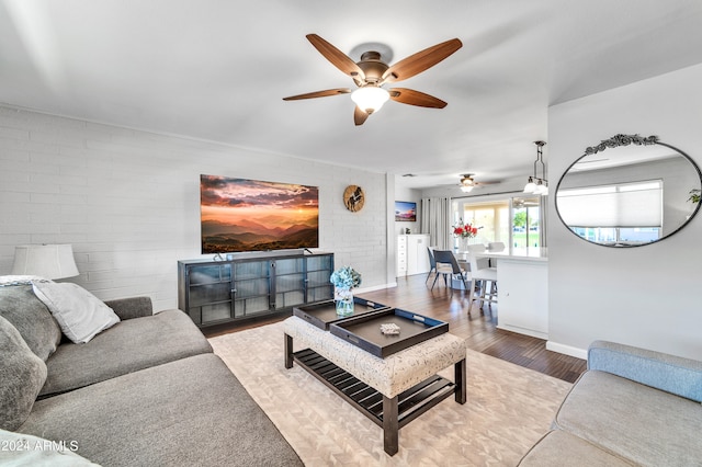 living room with brick wall, hardwood / wood-style floors, and ceiling fan