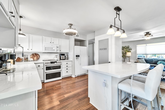 kitchen with decorative light fixtures, light stone countertops, white appliances, and white cabinetry