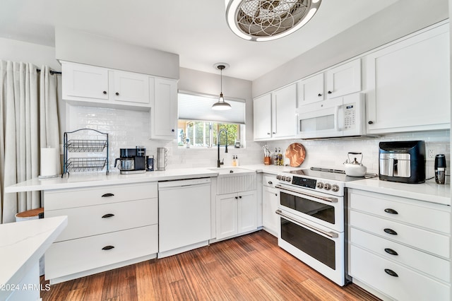 kitchen with light wood-type flooring, white appliances, sink, hanging light fixtures, and white cabinetry