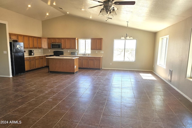 kitchen with dark tile patterned flooring, ceiling fan with notable chandelier, pendant lighting, black refrigerator, and a center island