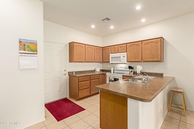 kitchen with white appliances, visible vents, a breakfast bar, a peninsula, and a sink